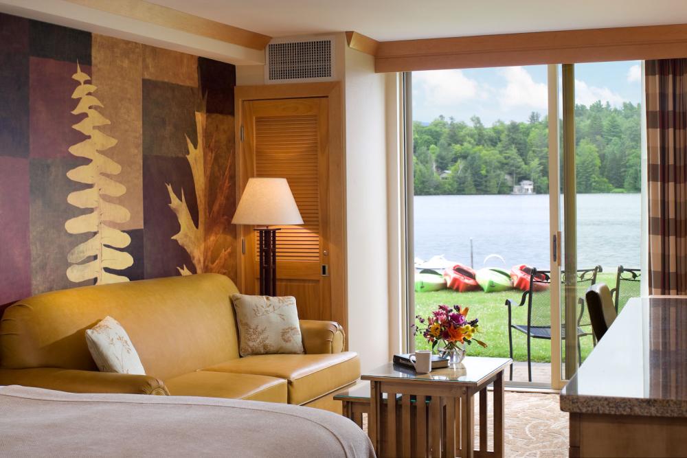 A hotel room with sliding doors opening onto a lakefront lawn with kayaks.