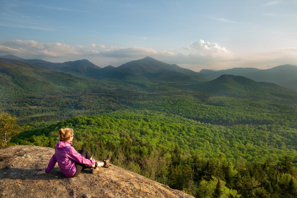 A hiker sits atop a rock, overlooking the mountain range.