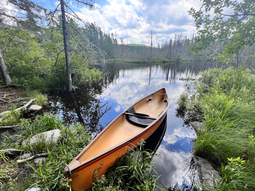 A light brown lightweight canoe at a launch on a backcountry river.