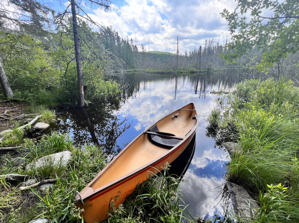 A  light brown lightweight canoe at a launch on a backcountry river.