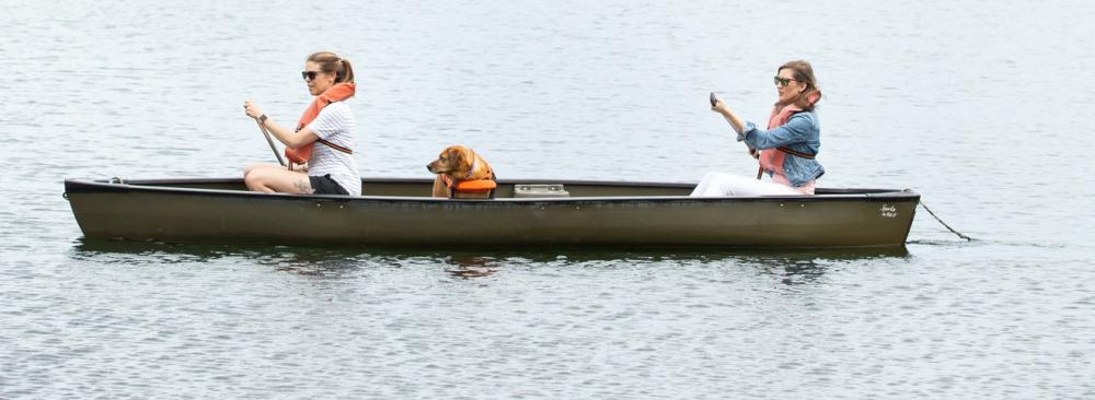 Two women and a dog in a brown canoe.