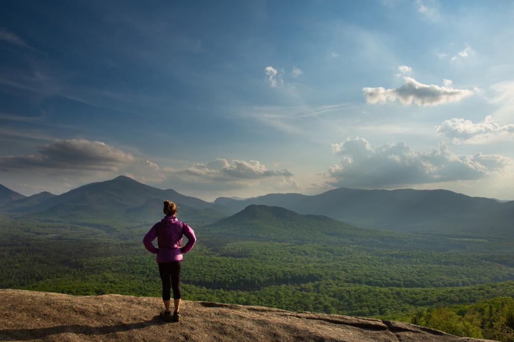 A hiker looks over the view at a mountain's summit