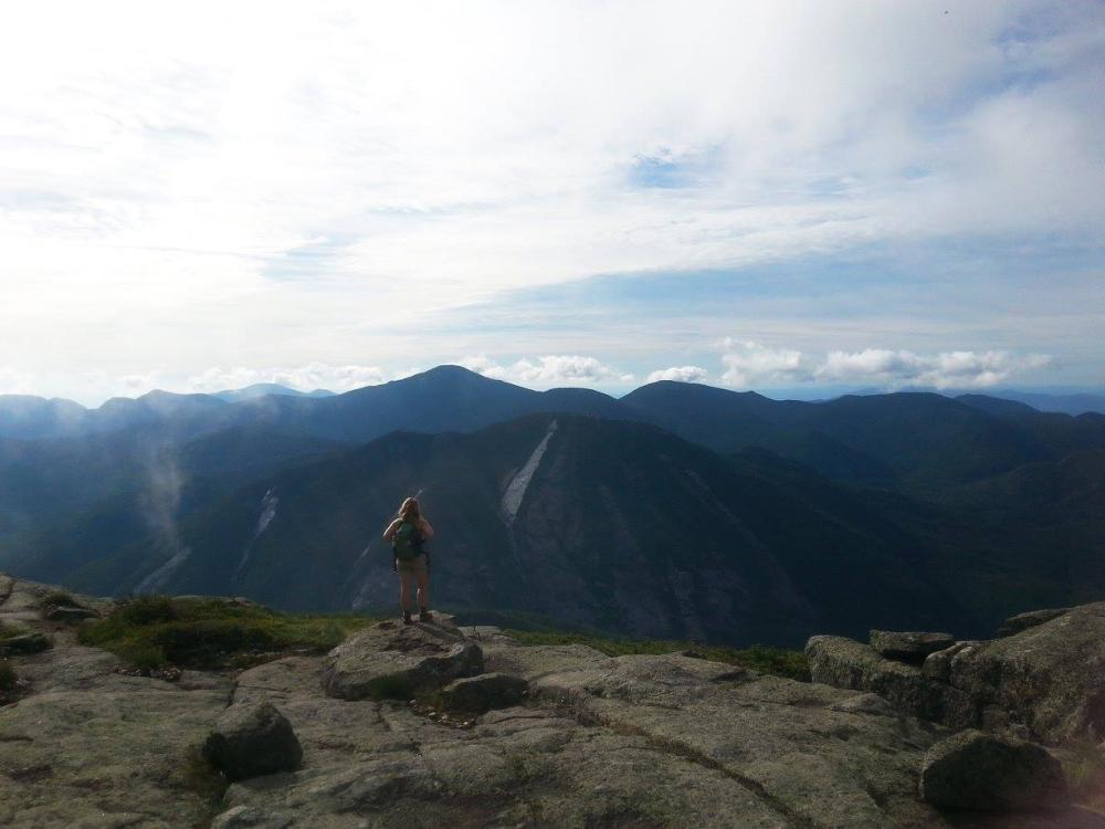 The author standing on Algonquin. A woman with hiking backpack stands admiring the view in the High Peaks.