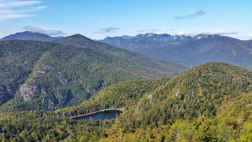 An early fall day in the High Peaks. Do you recognize any mountains? Green leaves, just starting to change to fall colors, make up most of this mountain view.