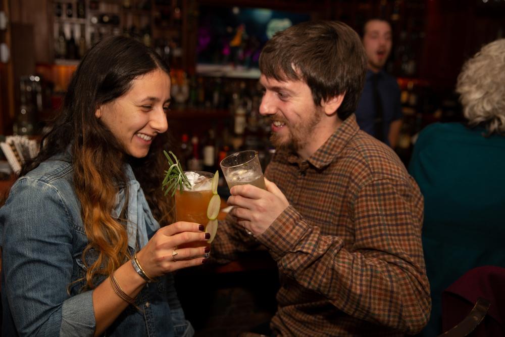 A couple holds cocktails at a bar.