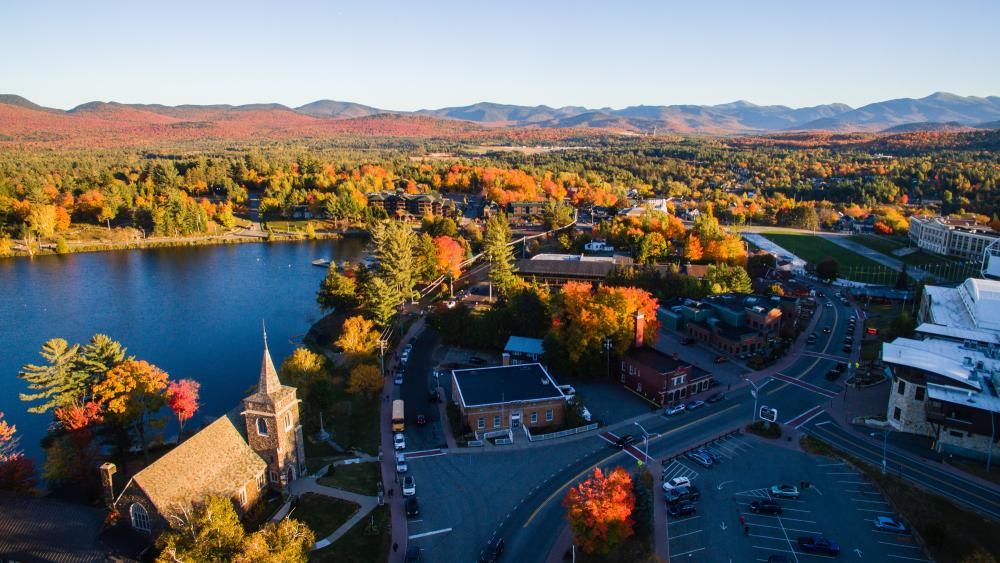 Aerial view of Lake Placid. Trees with fall foliage. Main street. Mirror Lake. Mountains in the background.