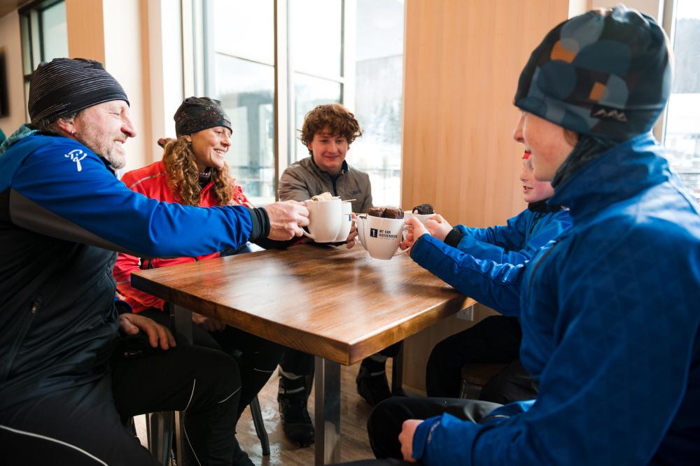 A family drinks hot cocoa at a table next to a snowy window.