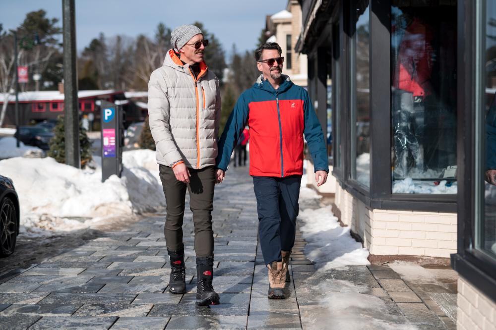 Two men walk on Lake Placid Main Street in winter on a sunny day.