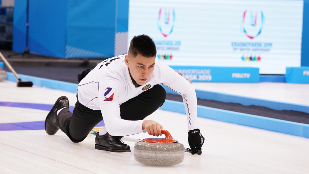 A male curler slides on ice, pushing a curling stone.