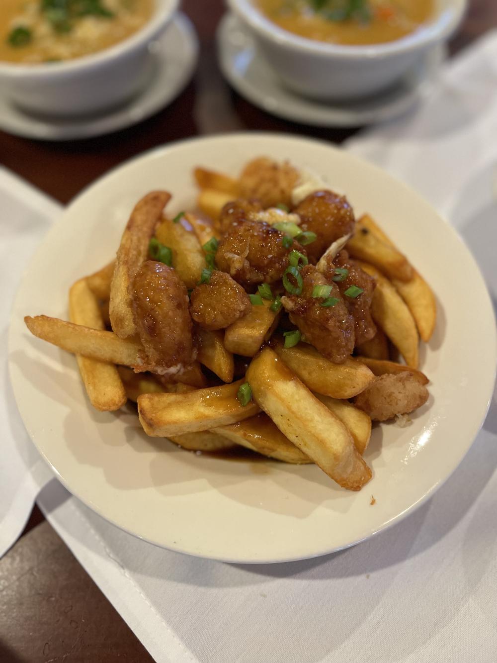 Extreme close-up of a dish of glazed, fried cheese curds on a bed of French fries.