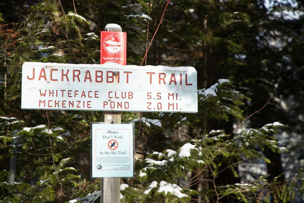 A carved wooden trail sign for the Jackrabbit Trail shows distances to the Whiteface Club and McKenzie Pond.