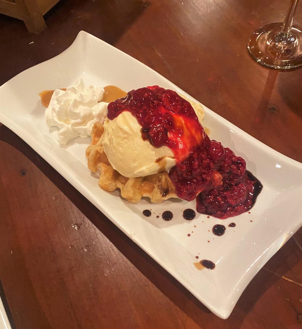 A lavish dessert of waffle, ice cream, caramel, and raspberry sauce.