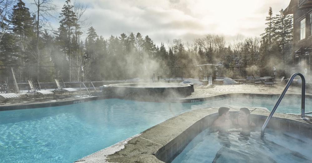 Two people sit in the water on a winter's day as steam rises from the outdoor swimming pool at the Whiteface Lodge