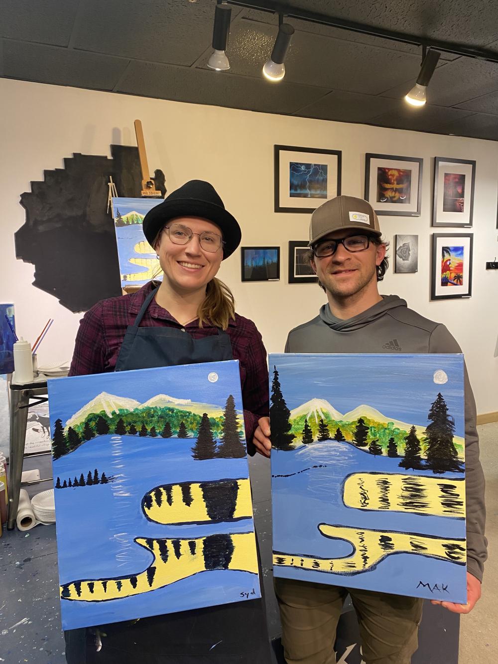 A man and a woman hold up paintings, each a version of the same image, from an art class.