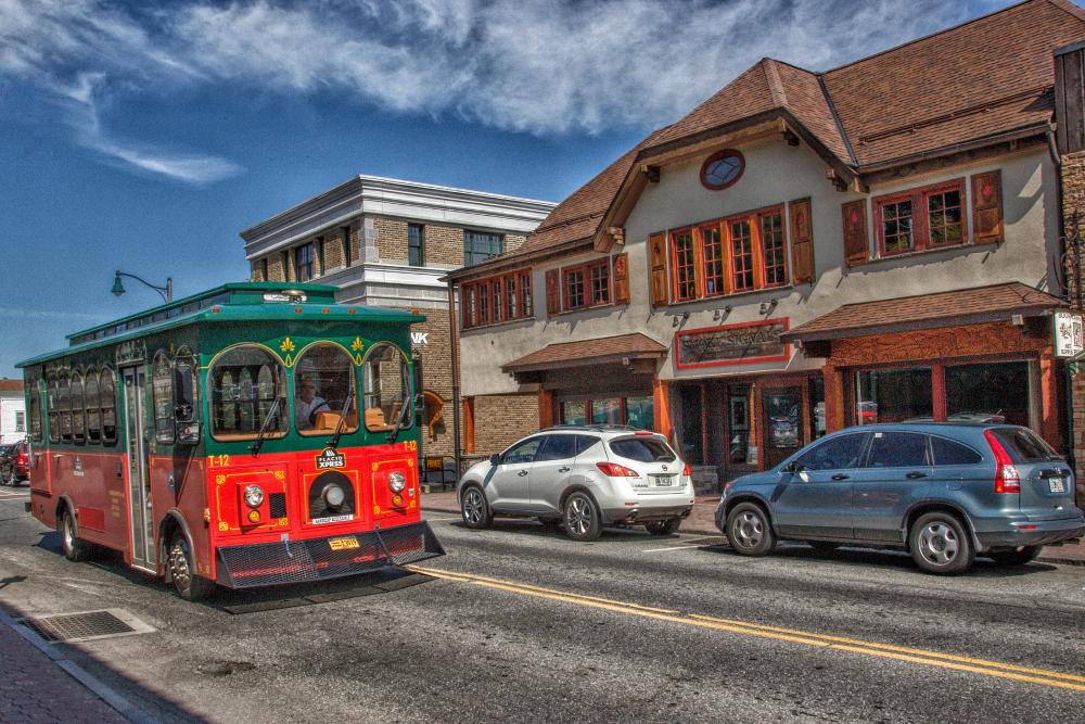 A trolley bus drives on a quaint street past a barbecue restaurant.