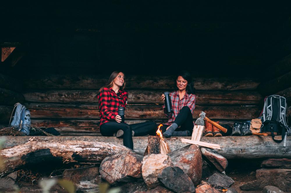 Two women in flannels talk in a lean-to.