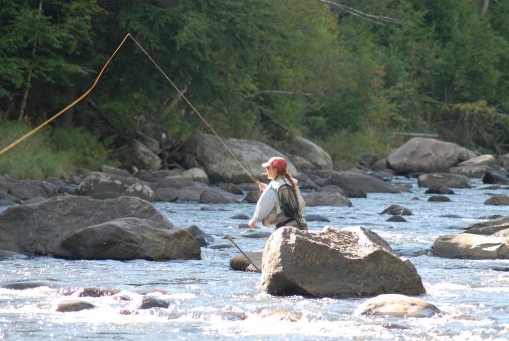 A woman casts a fly fishing lure in a stream.