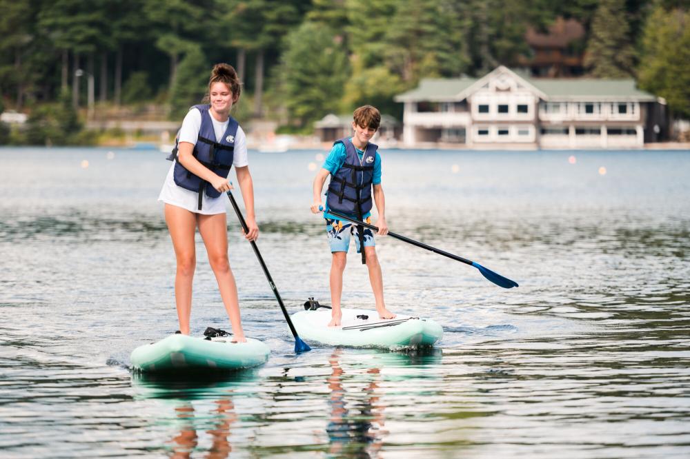 Two kids paddle on SUPs on Lake Placid.