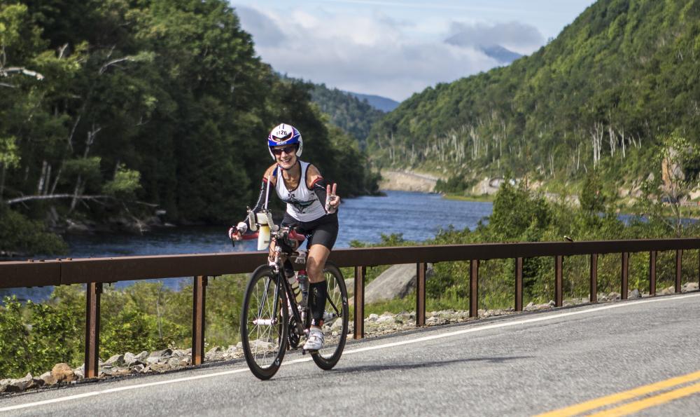 a woman rides her bike and throws up a peace sign in front of a rushing river.