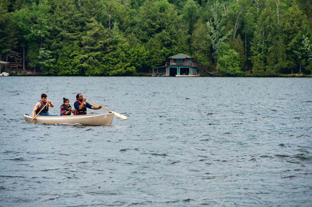 A man paddles with two passengers in a canoe.