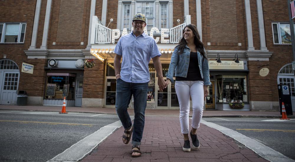 A man and woman hold hands crossing a street with a brightly-lit old fashioned movie marquee behind them.