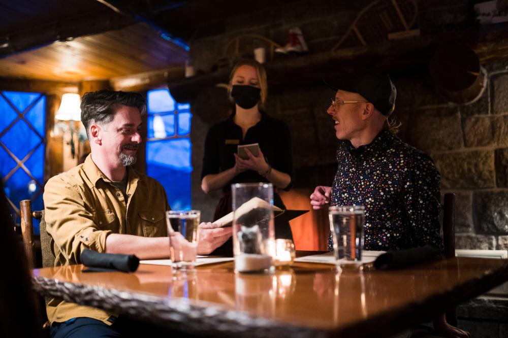 Two men smile while ordering food at a romantic, dimly lit restaurant.