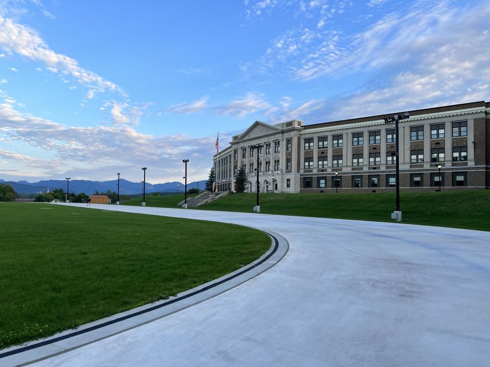 A stone high school overlooks a smooth skating track on a summer day.
