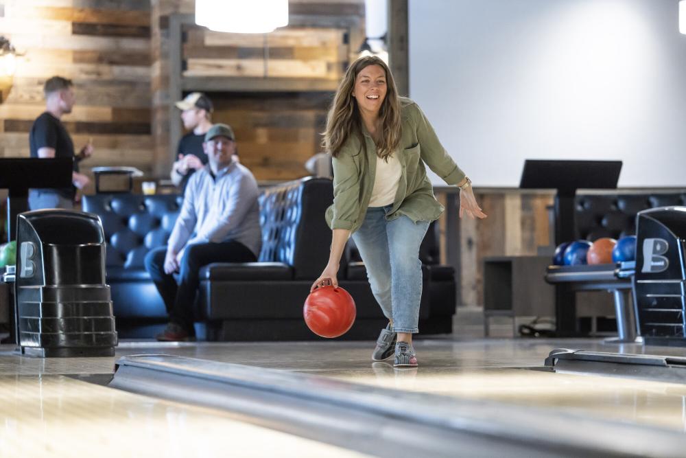 A woman prepares to release a bowling ball on a wood alley at a hip bowling alley.