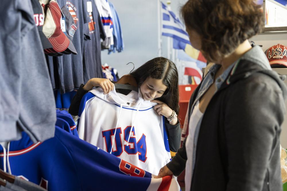 A young woman holds a USA hockey jersey up to herself in a brightly colored shop.