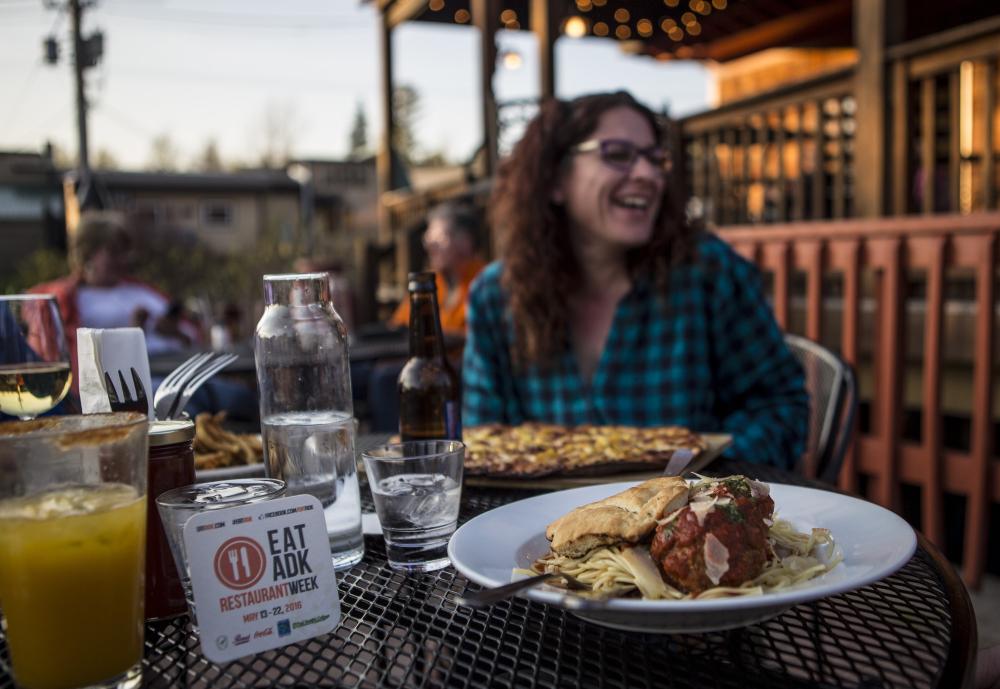 A woman laughs with food on a patio.