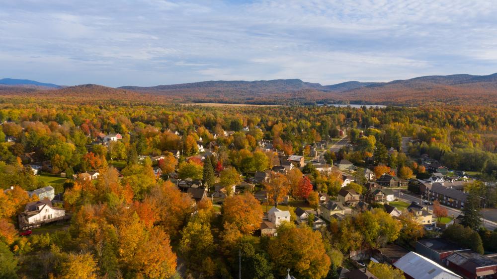 Downtown Tupper Lake with mountains in the back covered in fall reds and yellows.