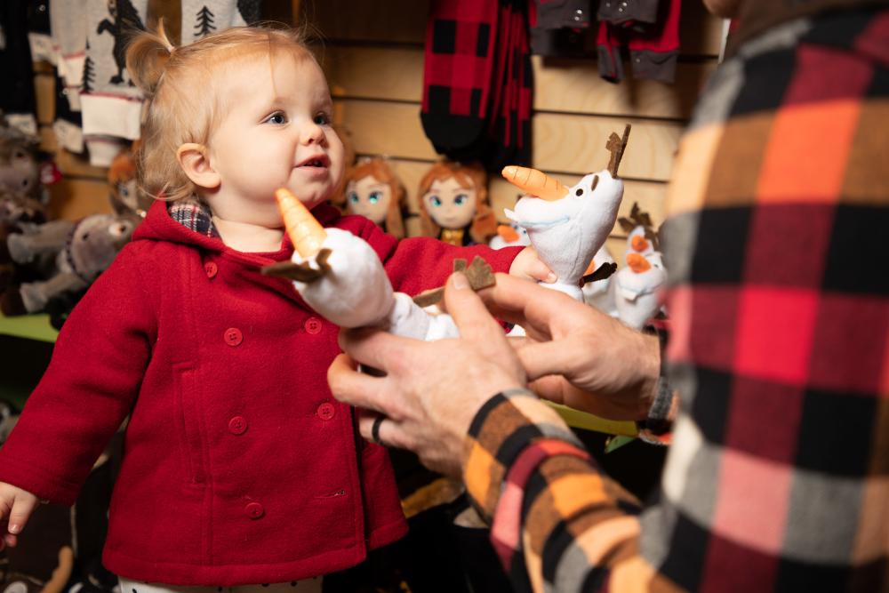 A toddler reaches out to a stuffed animal in a shop.