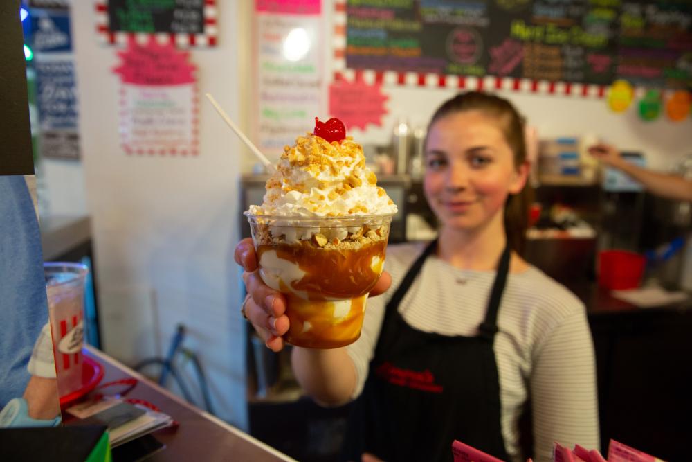 A woman holds up a caramel sundae at an ice cream shop.