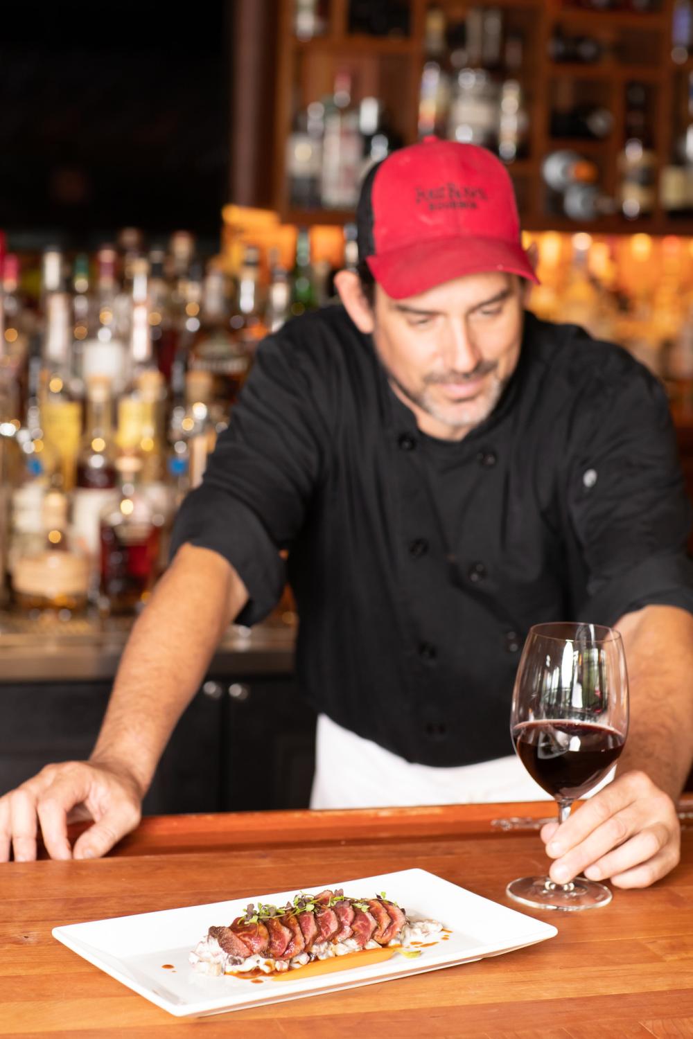 A man stands at a bar with tuna and a drink.