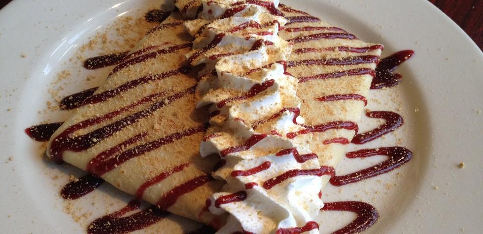 A crepe with whipped cream and strawberry jam striped on top.
