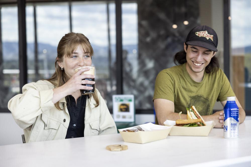 A man and woman enjoy coffee and sandwiches on a deck.