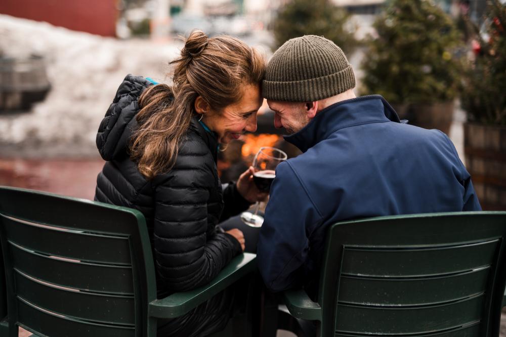 A man and woman share wine in Adirondack chairs.