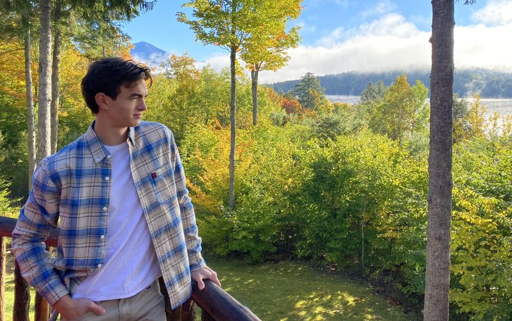 A young person wearing a flannel shirt poses and looks off into a forest glowing with golden light