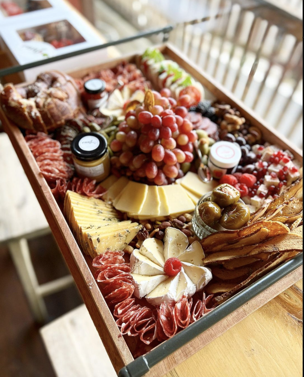 A charcuterie board with an assortment of meats, cheeses, peppers, grapes, mustard, bagel chips and more
