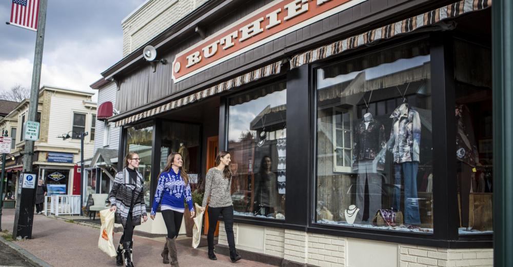 Three people walk on the Lake Placid sidewalk carrying shopping bags