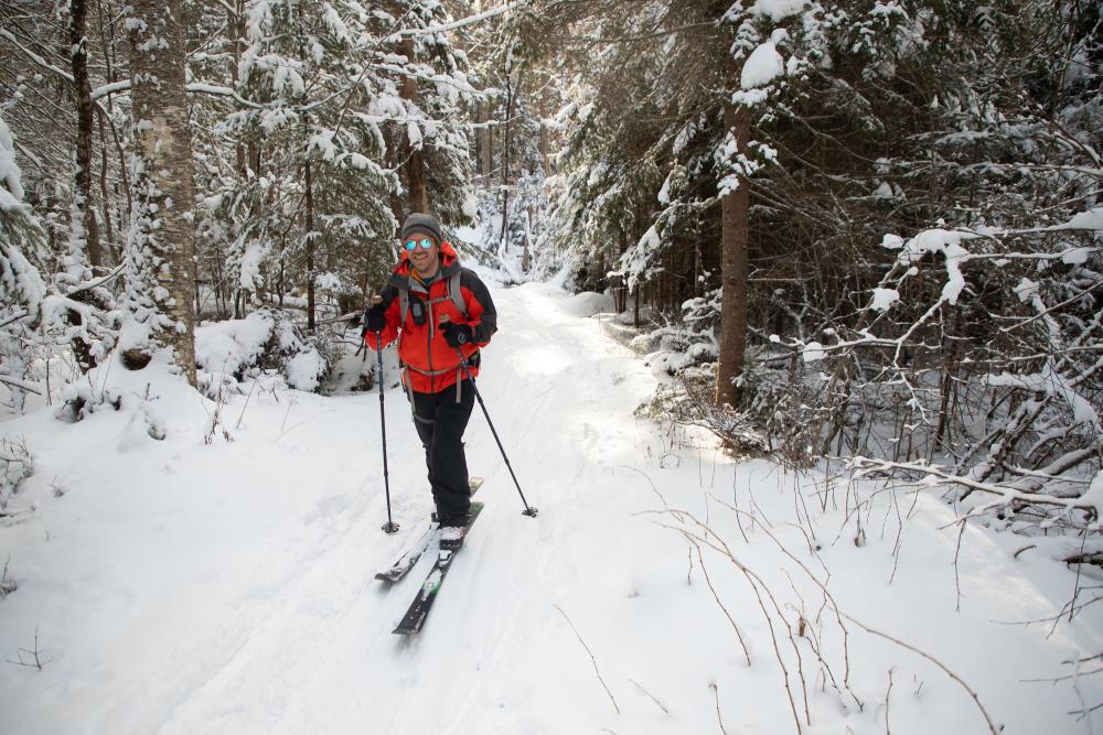 A man smiles as he cross-country skis through a snowy trail.