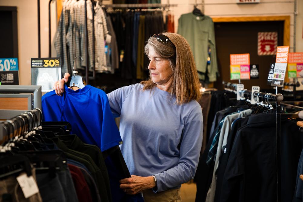 A woman contemplates buying a blue t shirt in a store.