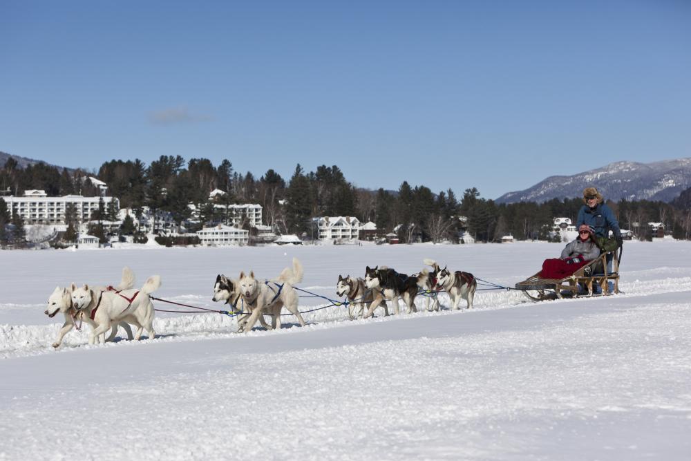 A couple rides in a dog sled on a frozen lake.