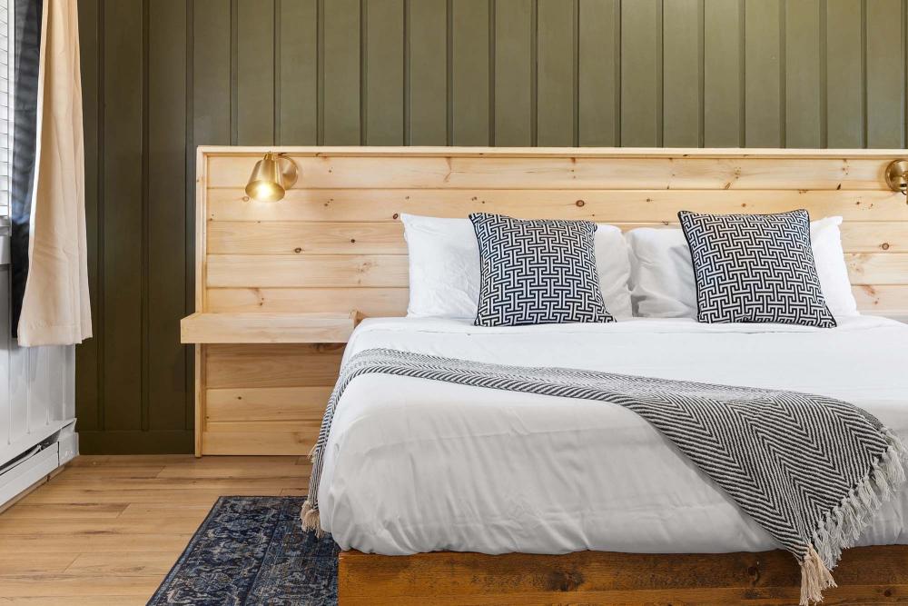 A white bed next to a green wall in a simply decorated room.