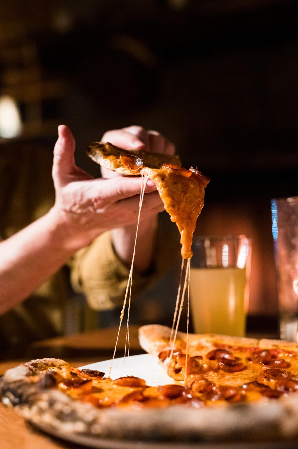 A man's hand holds a slice of wood-fired pizza