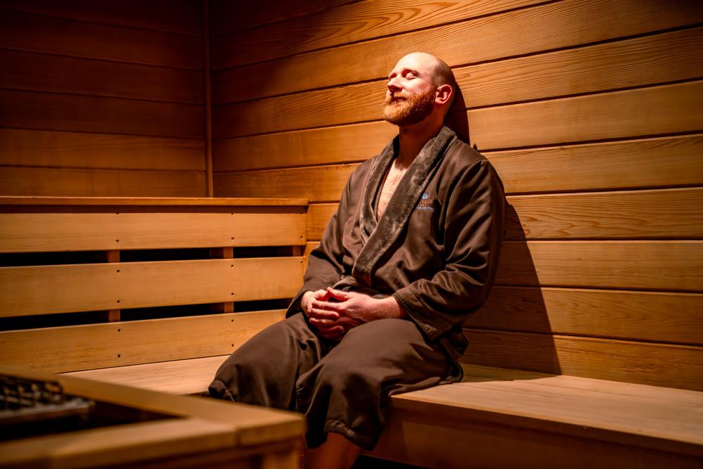 A man wearing a spa robe relaxes with his eyes closed in a sauna