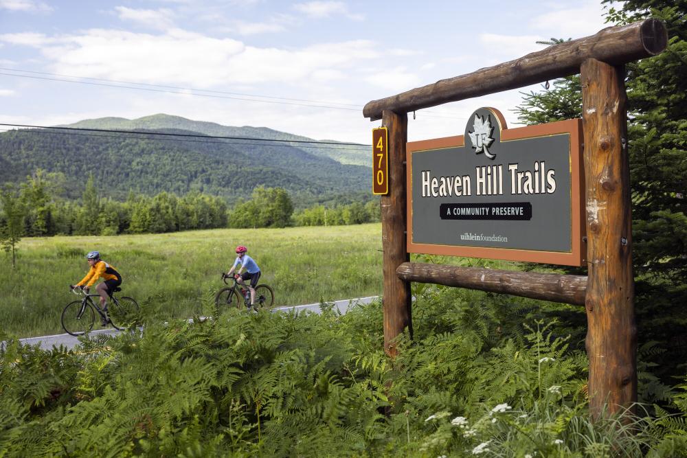 Two people on bikes ride past the Heaven Hill Trails sign.