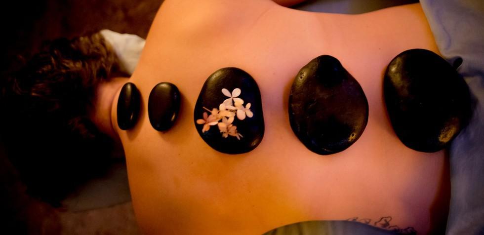 A woman lies on a spa table with hot stones in a line down her back.