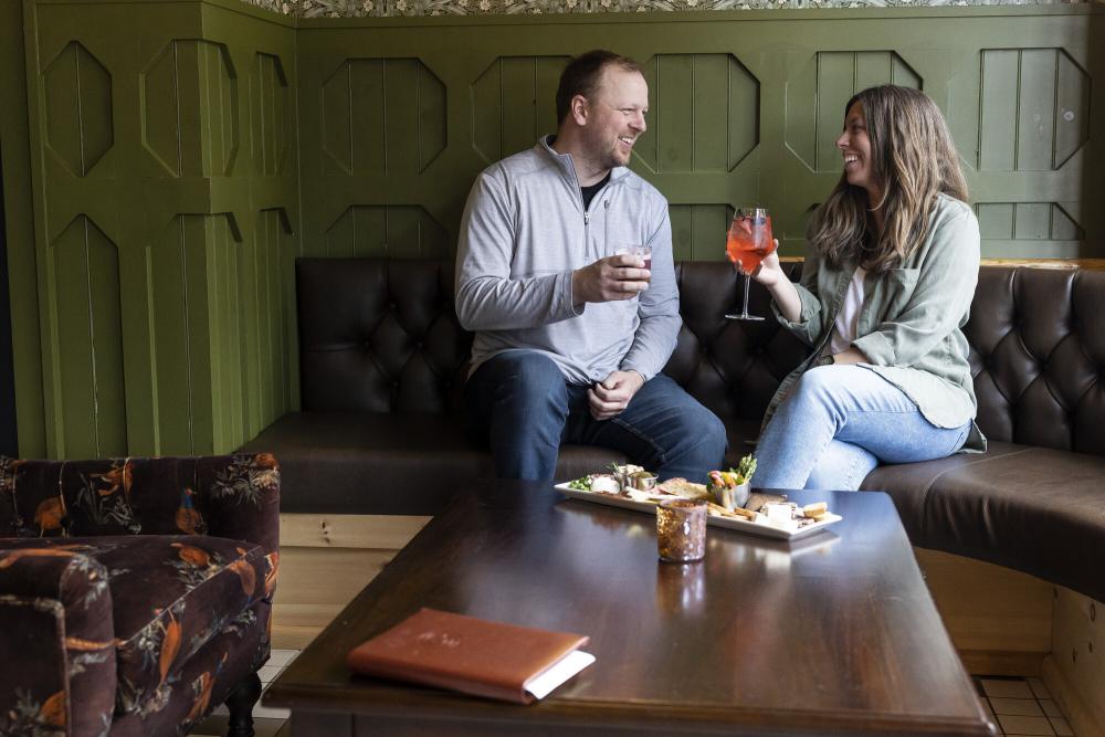 Couple sits on bench seat with cocktails and food on table