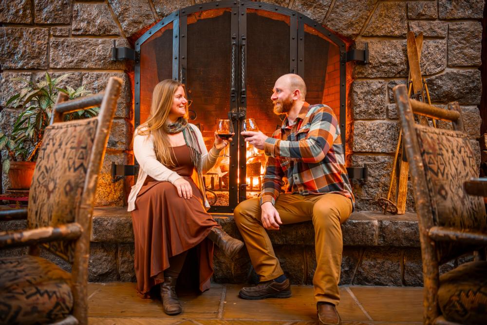 Fireside Drinks at Whiteface Lodge Man and woman cheers glasses sitting in front of stone fireplace